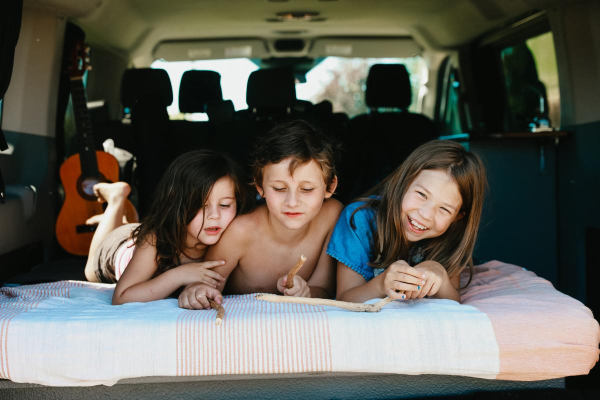 three children laying on a bed in the back of a van.