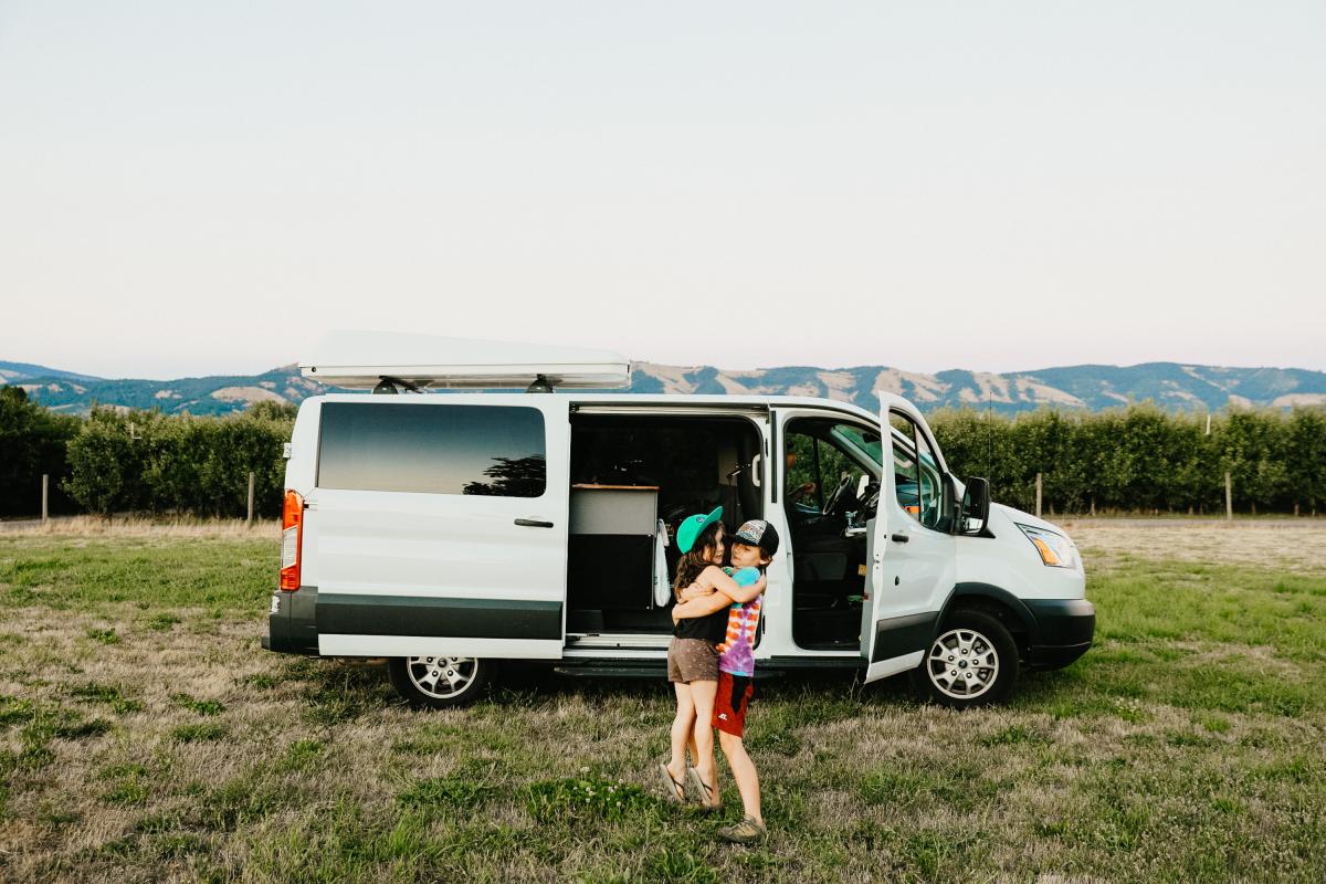 a girl standing next to a van in a field.