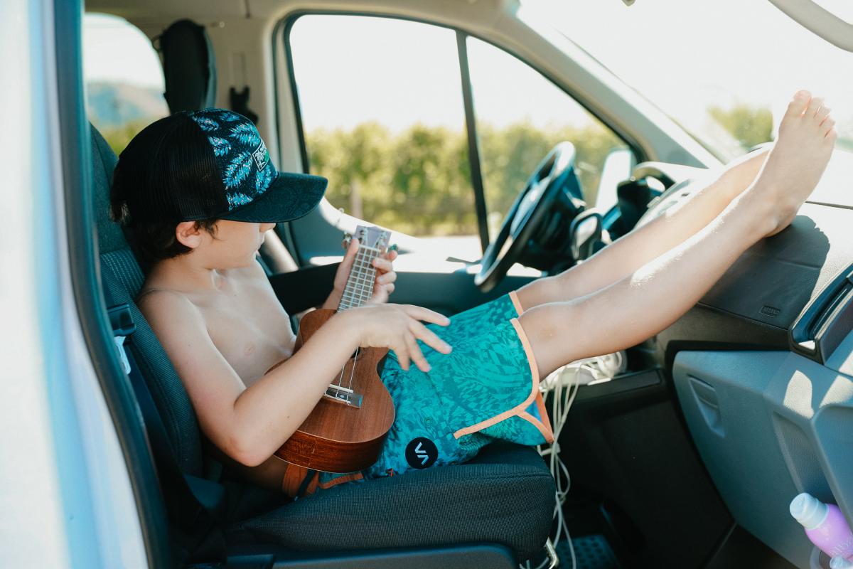 a boy sitting in the back seat of a van playing an ukulele.