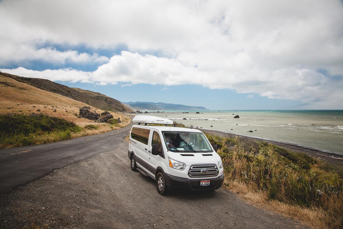 a van is parked on a dirt road near the ocean.