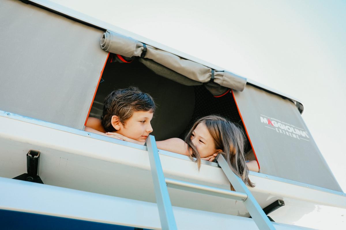 camping with two children looking out of the window of a rooftop tent on a camper van