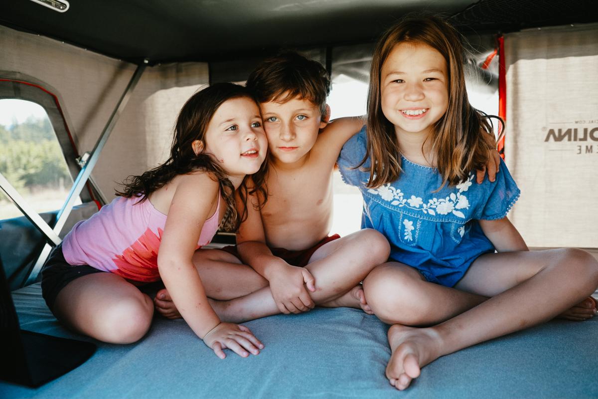 three kids sitting in the back of a camper.