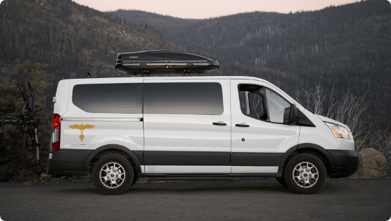a white van with a roof rack parked in front of mountains.